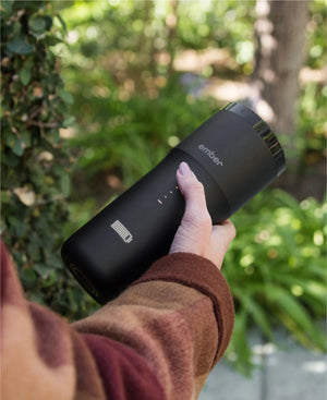Electric Coffee Travel Mug black V2 - 355ml wordt buiten vastgehouden met groene achtergrond.