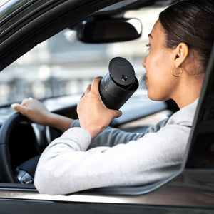 Persoon drinkt koffie uit een zwarte thermosbeker met schuifdeksel in de auto, onderdeel van Take away, Fellow, EspressoGear, alles over koffie.