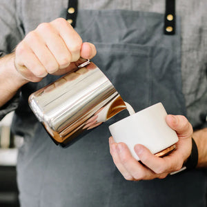 Barista schenkt melk uit een gepolijste kan van roestvrij staal, onderdeel van Espresso Accessoires en Melkkannen, alles over koffie.