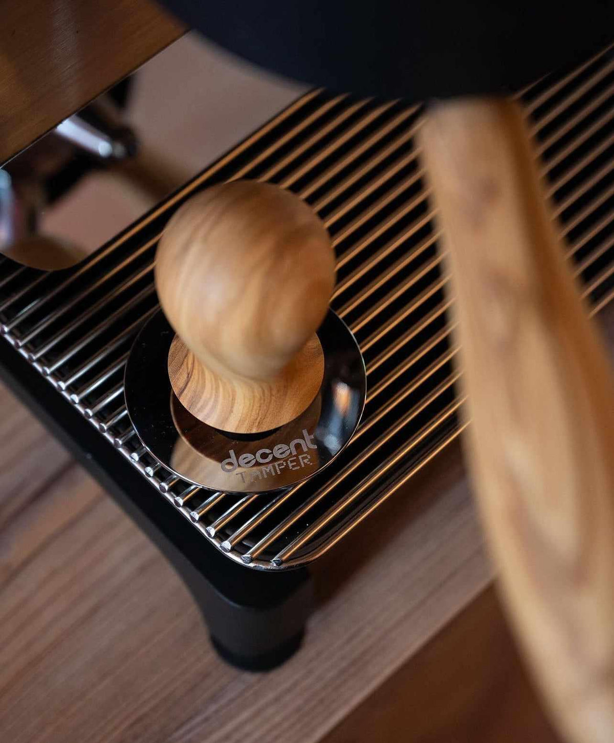 Närbild på en kaffetamper med trähandtag placerad på en metallgallerhylla på en kaffemaskin i trä och metall.