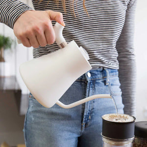Hand die water schenkt uit een witte waterkoker met smalle tuit in een koffiefilter, onderdeel van EspressoGear, alles over koffie.