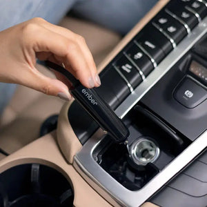 Hand die autolader voor Ember elektrische mok aansluit op de sigarettenaansteker van de auto voor gemakkelijk opladen.